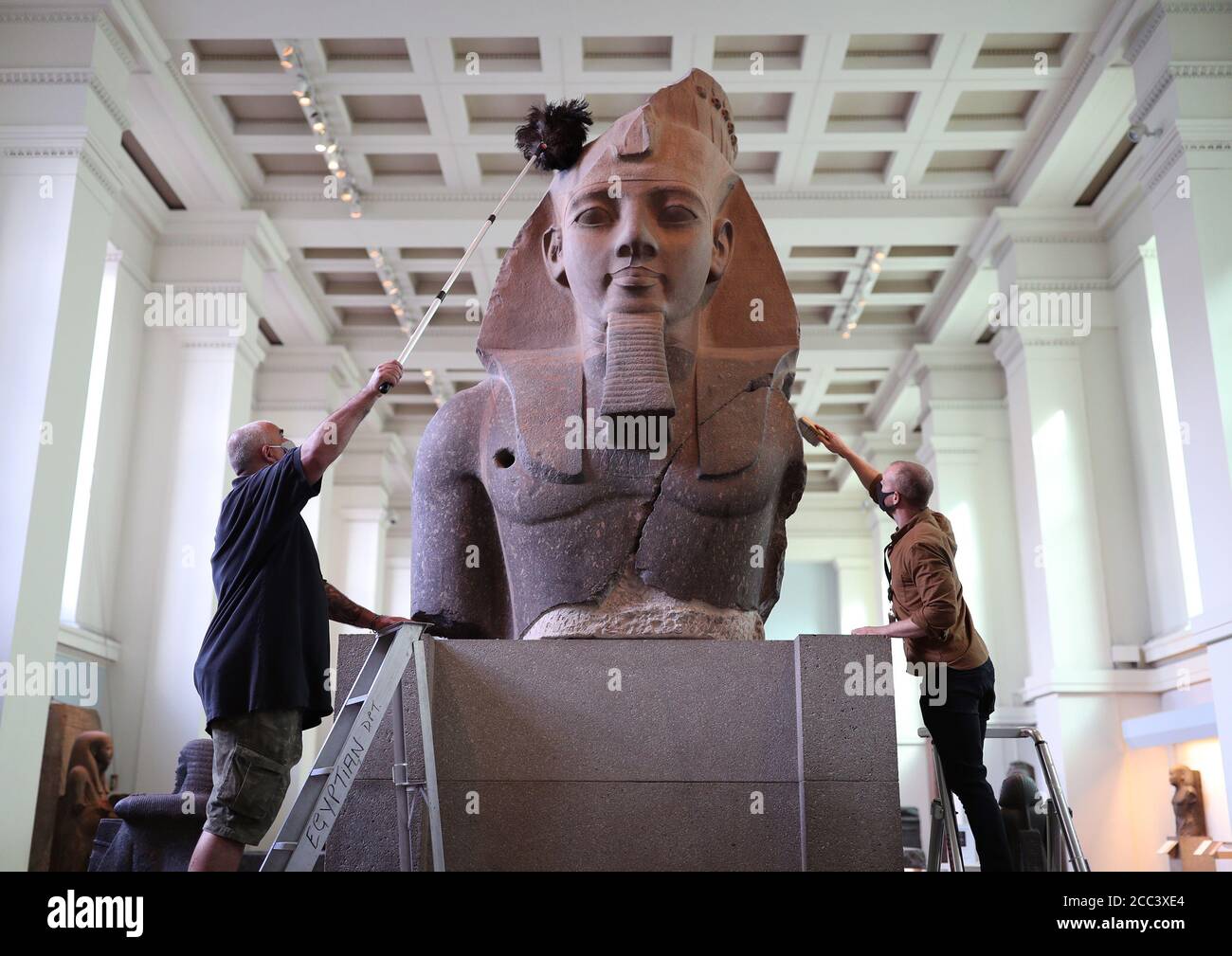 I manager della collezione Evan York (a sinistra) e Alex Truscott spolverano la parte superiore di una colossale statua seduta del re Ramesses II (circa 1279-1213 a.C.), nella Egyptture Gallery del British Museum di Londra, mentre si preparano a riaprire al pubblico il 27 agosto dopo il blocco del coronavirus. Prima della riapertura, il British Museum ha avviato il più grande programma di pulizia individuale degli ultimi decenni. Foto Stock