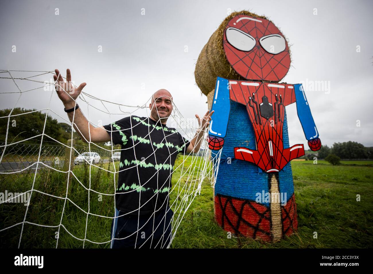 Robert Slattery di Dublino si pone nella rete di un 12ft (3,65m) di Spider-Man progettato da Shauneen Kilpatrick, e costruito con fieno in un campo al largo della circonvallazione di Newtownstewart in Co. Tyrone dal Festival della Comunità dei due Castelli. I supereroi della fieno NHS sono lì per ricordare alla gente che "insieme siamo un super potere" nella lotta contro il coronavirus. L'attrazione raccoglie denaro per la carità e promuove il festival locale. Foto Stock