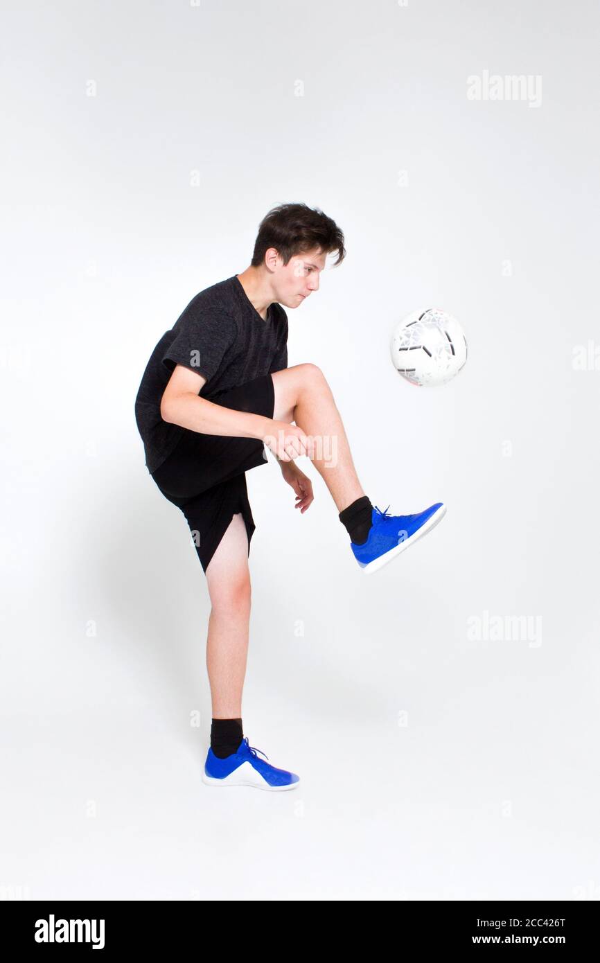 Un ragazzo in una t-shirt sportiva nera e shorts, sneakers blu, allenano e gioca con una palla da calcio. Foto Stock