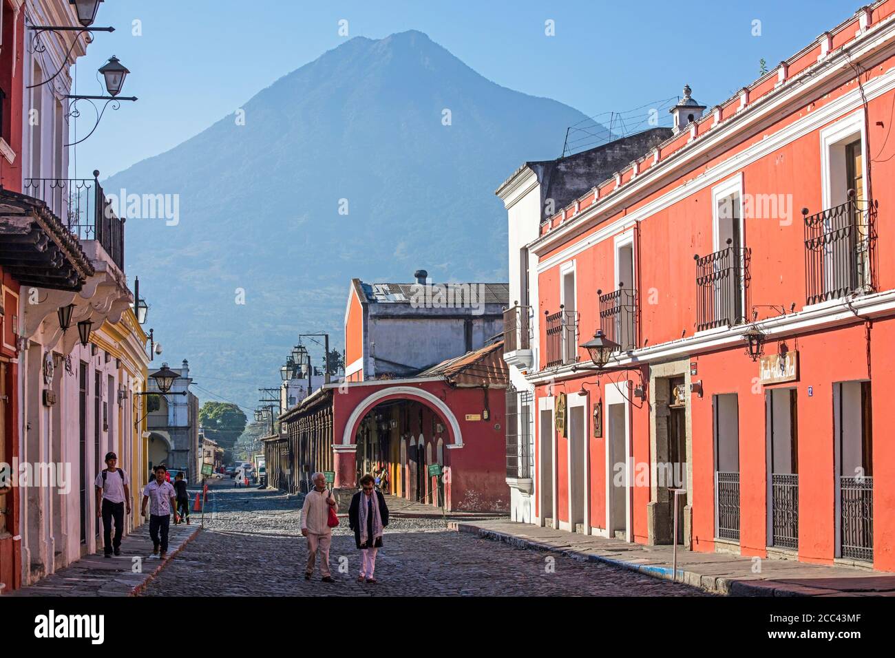 Volcán de Fuego e i turisti occidentali camminano in strada con case coloniali colorate nella città di Antigua Guatemala, Dipartimento Sacatepéquez, Guatemala Foto Stock