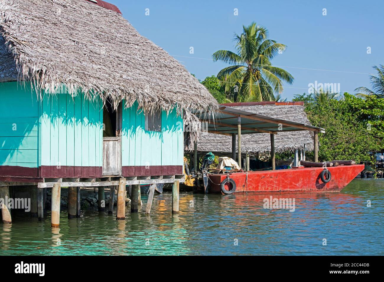 Barca rossa e casa di legno su palafitte con tetto di paglia sul fiume Dulce / Rio Dulce, Izabal Dipartimento, Guatemala, America Centrale Foto Stock
