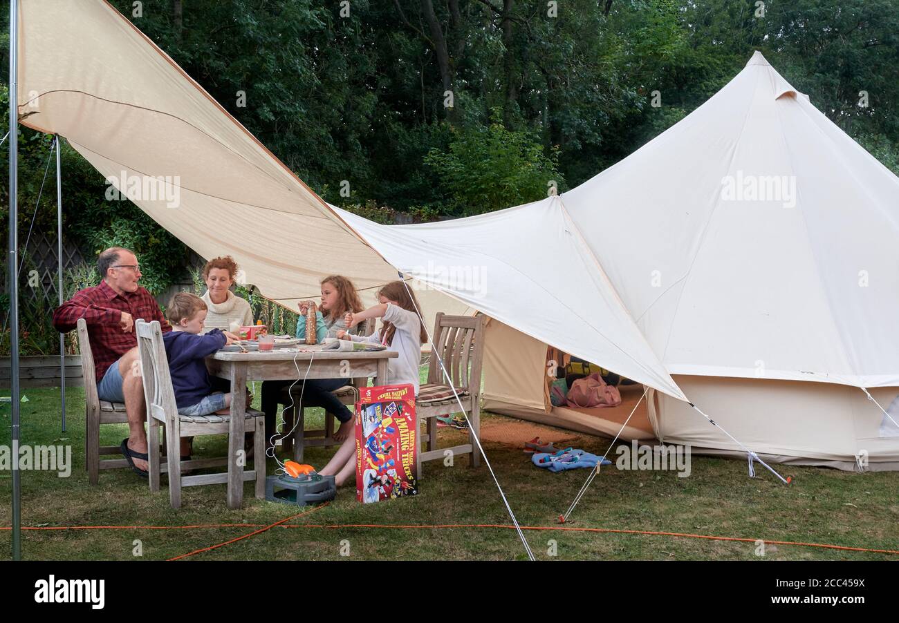 Una famiglia di cinque ha un pasto sotto la loro tenda awnng in un giorno piovoso nella loro vacanza di giardino di staycation durante la crisi del coronavirus, estate 2020. Foto Stock