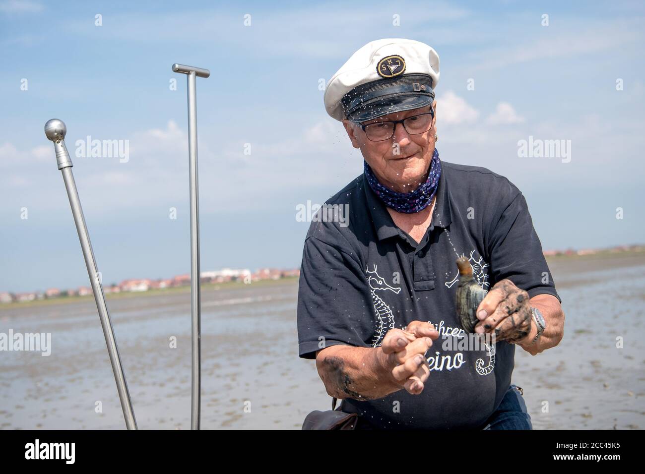 Juist, Germania. 14 agosto 2020. Heino Behring, guida fangflat, mostra come l'acqua spruzzi da una vongola di sabbia. Anche da ragazzino, l'età di 72 anni era sulla sua strada nei mudflats prima di Juist. Per esattamente 40 anni, Heino ha condiviso le sue conoscenze sulle escursioni fangflat, e per molti turisti un tour con lui fa parte delle loro vacanze sull'isola. (A dpa: 'Una vita nelle mudflats - Wattführer Heino è ora in pensione') credito: Sina Schuldt/dpa/Alamy Live News Foto Stock