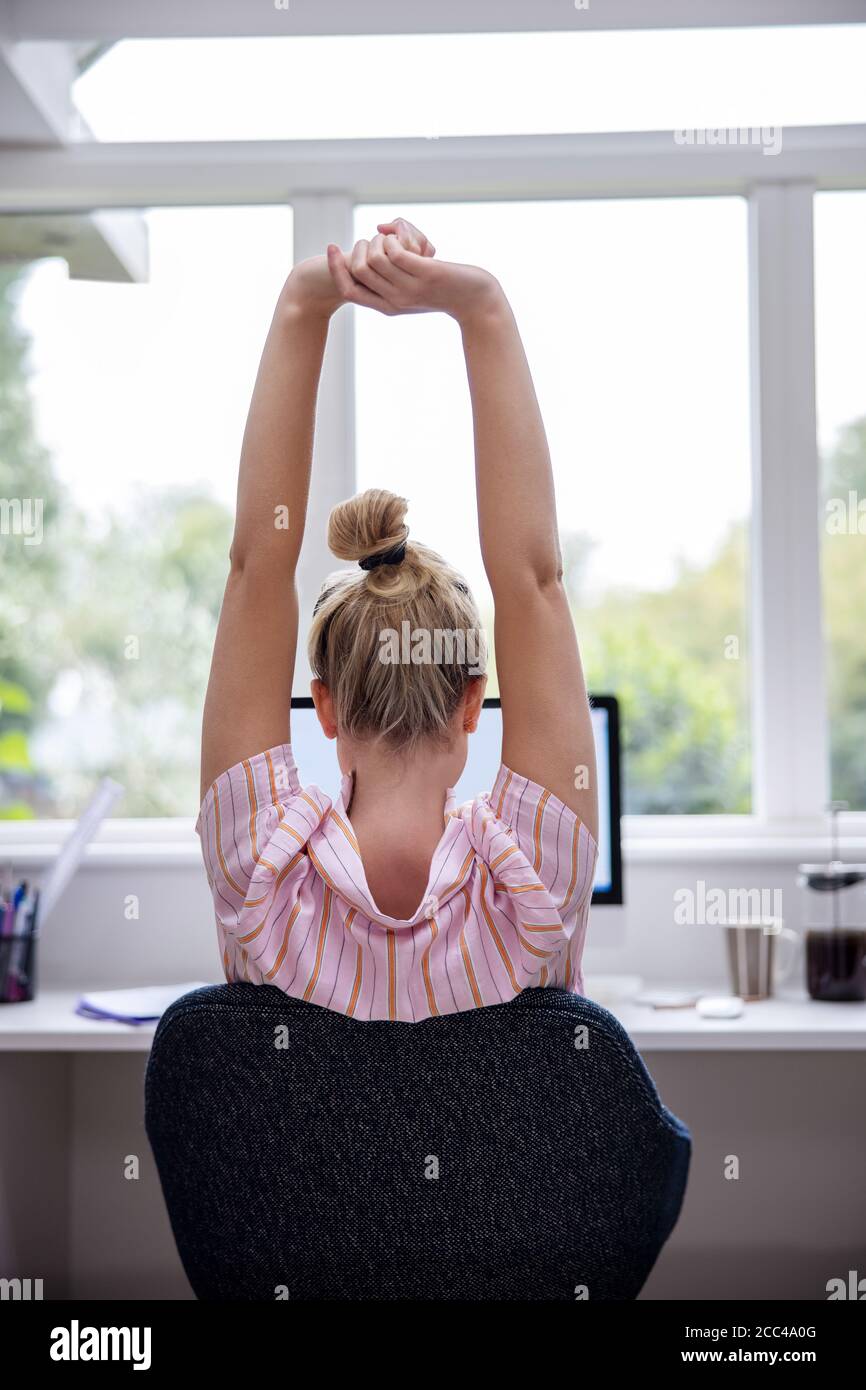 Vista posteriore di Donna che lavora da casa su computer in Home Office stretching alla scrivania Foto Stock