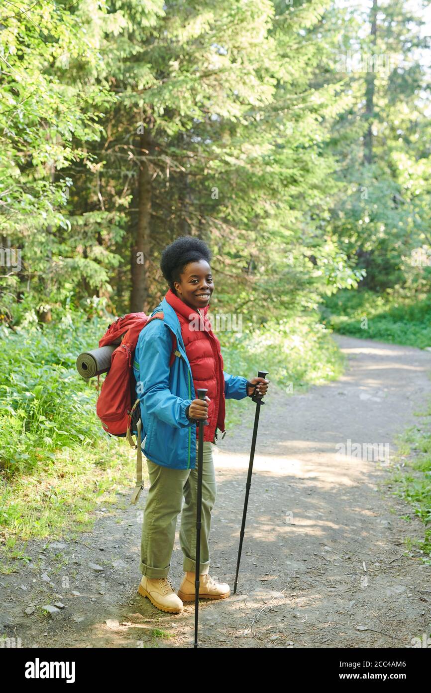 Ritratto di donna africana con zaino e bastoni sorridenti fotocamera mentre si è in piedi nella foresta Foto Stock