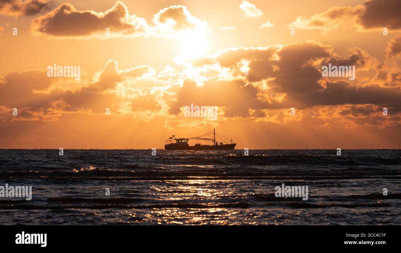 Trawler a nord vedere la costa durante il bellissimo tramonto dorato Foto Stock