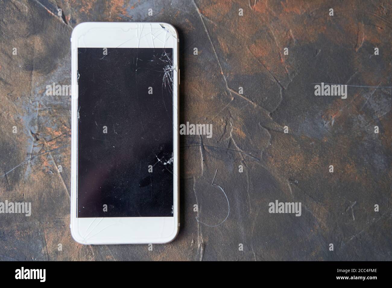 Telefono bianco con schermo rotto su sfondo scuro Foto Stock