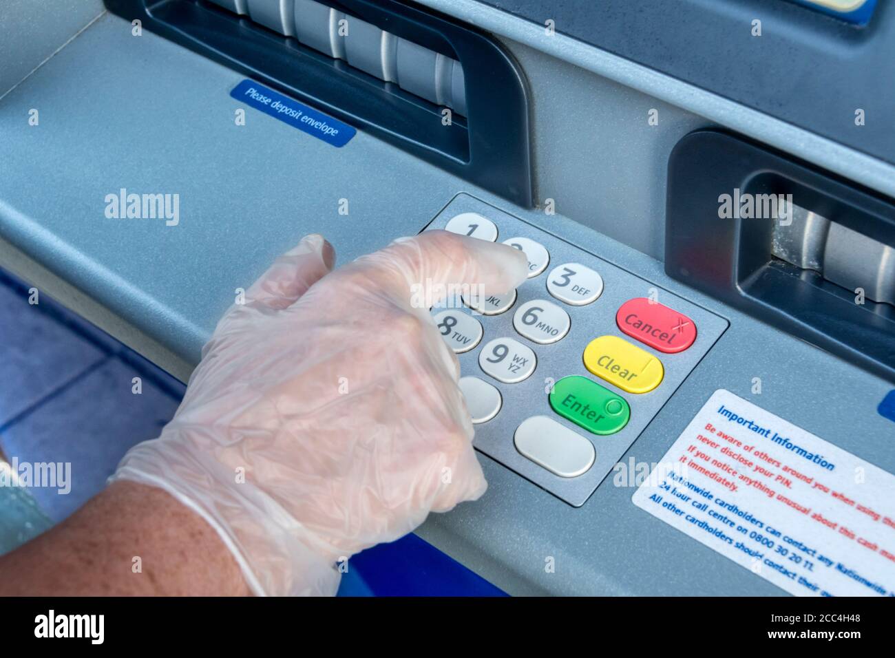 Donna che indossa guanto protettivo in plastica per azionare la cash machine durante 2020 coronavirus COVID-19 pandemia. Foto Stock