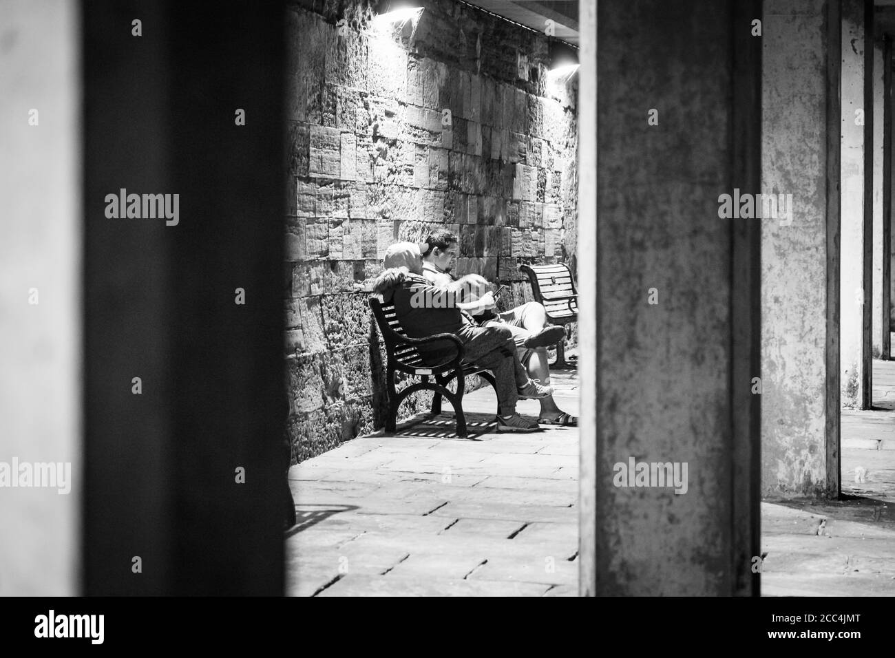 Un bianco e nero di una coppia sedeva su un panca sotto copertura di notte incorniciata da colonne di pietra Foto Stock