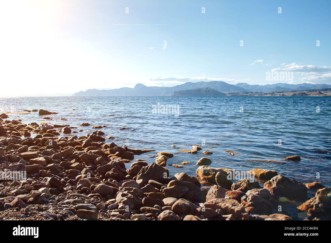 Mare spiaggia rocciosa sullo sfondo di cielo blu e montagne. Foto Stock