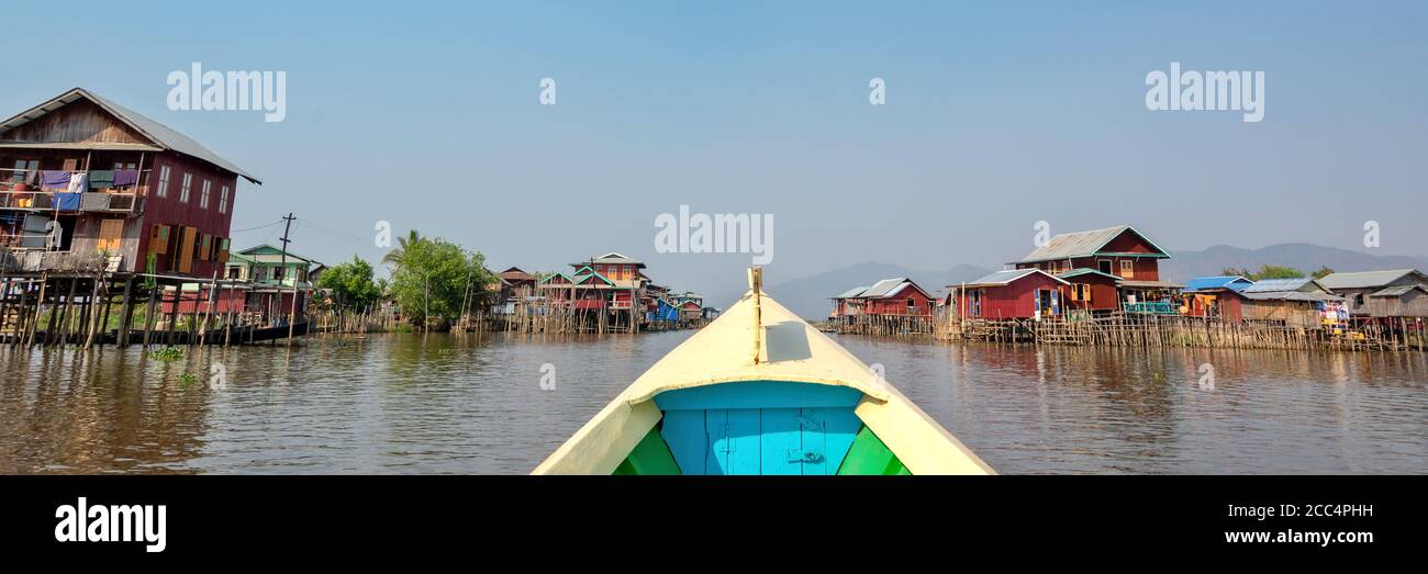 Barca che arriva in un colorato villaggio galleggiante con palafitte in Birmania, Myanmar Foto Stock