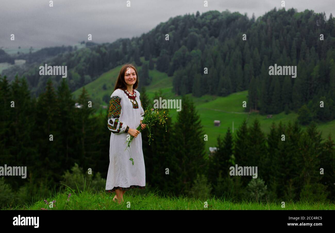 ragazza in ricamo con bouquet di fiori selvatici stand a piedi nudi su erba verde nelle montagne carpazi Foto Stock