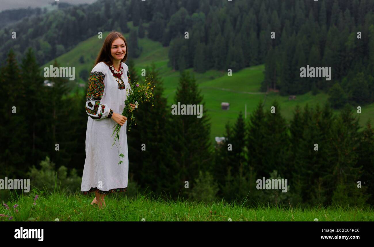ragazza in ricamo con bouquet di fiori selvatici stand a piedi nudi su erba verde nelle montagne carpazi Foto Stock