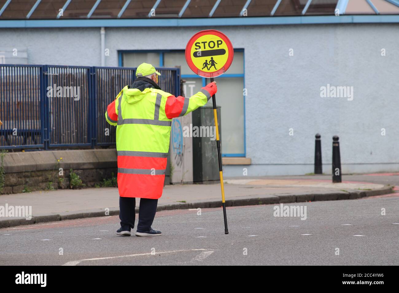 Lollipop uomo in piedi nel mezzo di un pedone traversata Durante l'orario di prelevamento a scuola Foto Stock