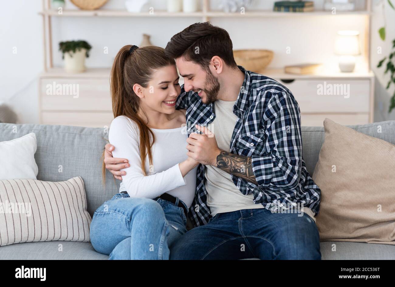 Felice insieme a casa. Felice giovane uomo e donna in abiti casual stanno tenendo le mani, abbracciando sul divano Foto Stock