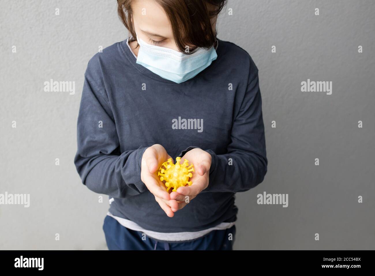 Ragazzo caucasico giovane che indossa una maschera chirurgica blu e tiene Un modello di virus corona durante la pandemia COVID-19 Foto Stock