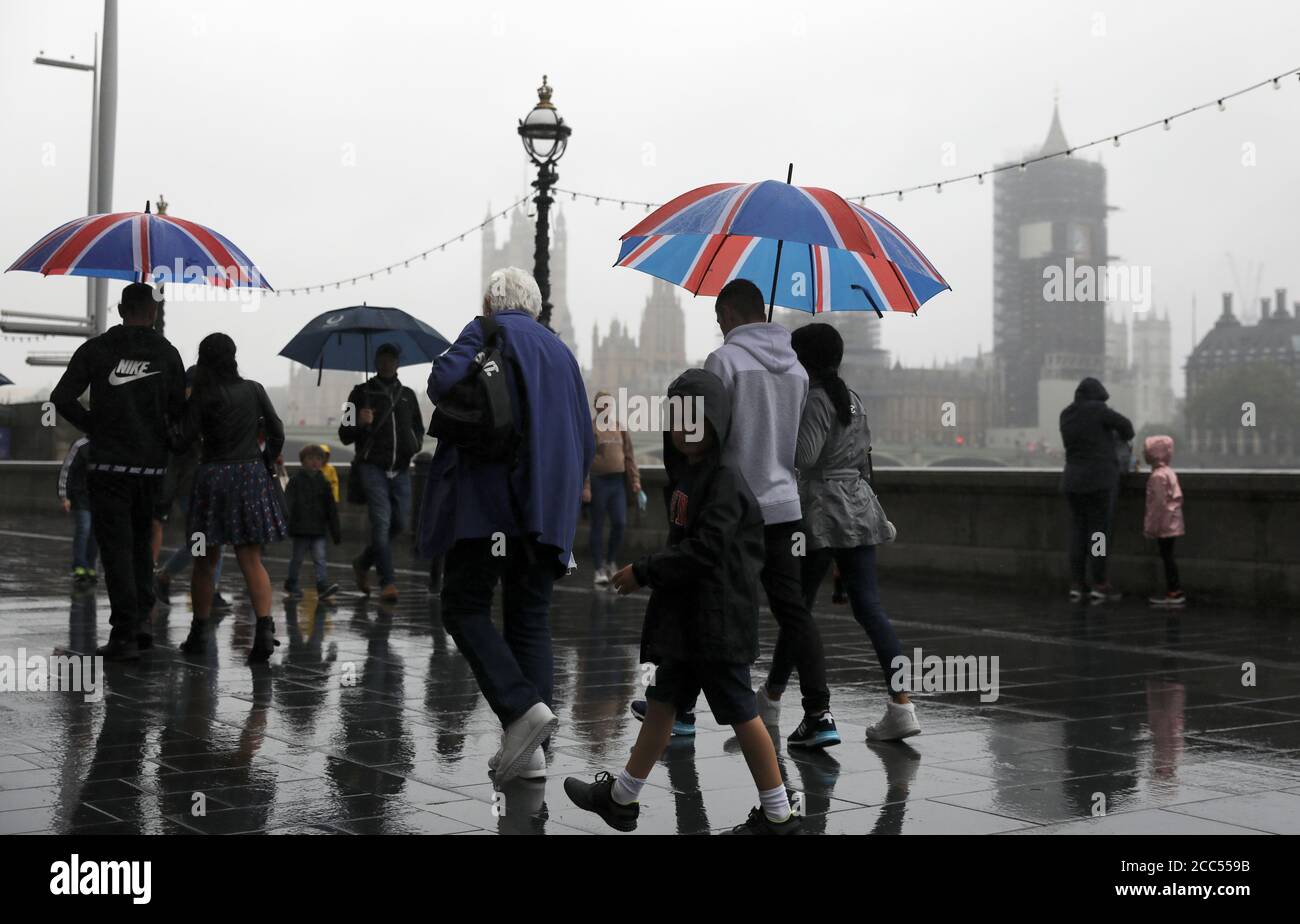 Persone con ombrelloni camminano sotto la pioggia alla Queen's Walk a Londra, Gran Bretagna 19 agosto 2020. REUTERS/Simon Dawson Foto Stock