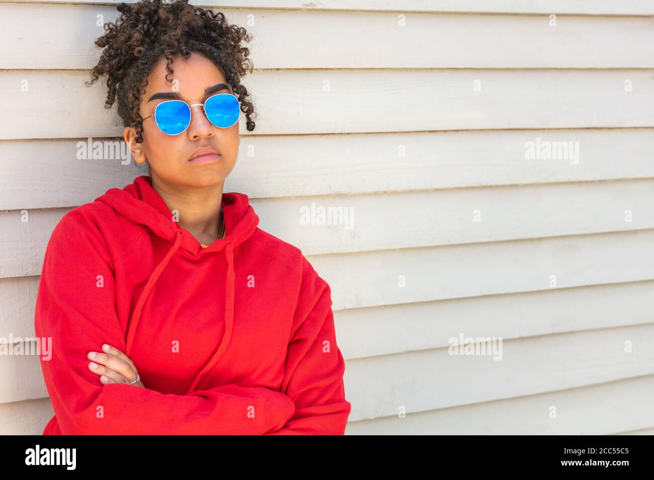 Ragazza adolescente cool teen misto razza biracial African American femmina giovane donna che indossa occhiali da sole blu e una felpa con cappuccio rossa vacanza al sole d'estate Foto Stock