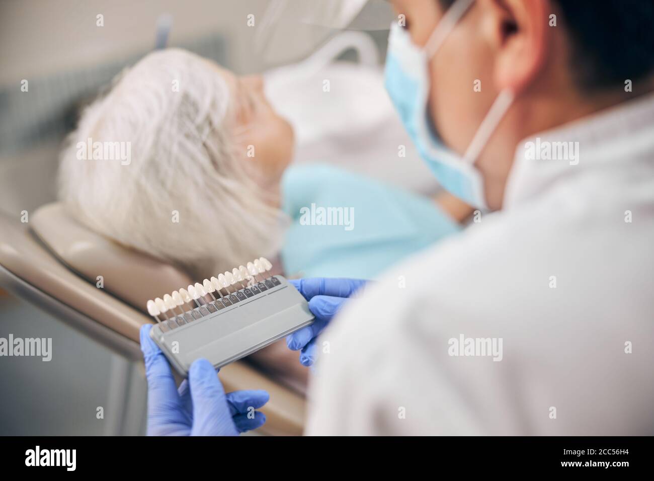 Dentista maschile che tiene in mano la tavolozza dei denti di colore per sbiancare in clinica odontoiatrica Foto Stock