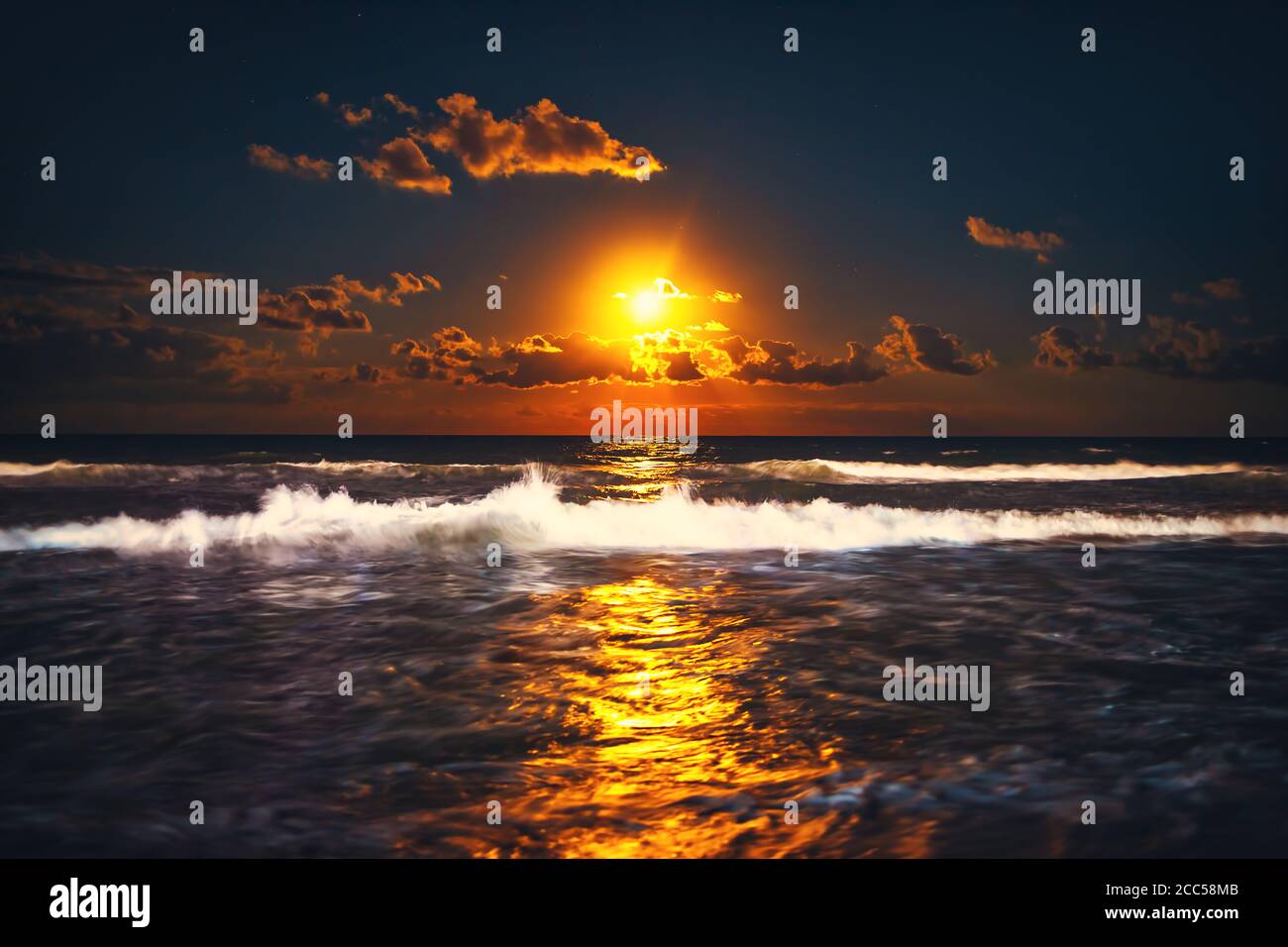 Luna piena che si innalza sulle onde del mare. Spettacolare tramonto sulla spiaggia. Foto Stock