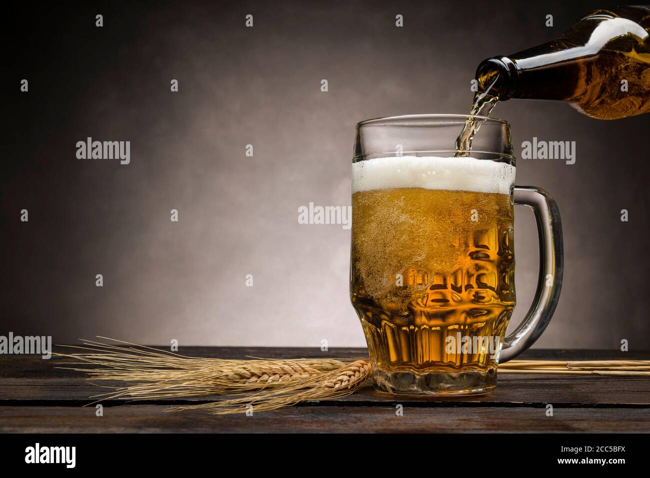 versare la birra bionda in una tinta di vetro su un tavolo di legno con orecchie di grano Foto Stock