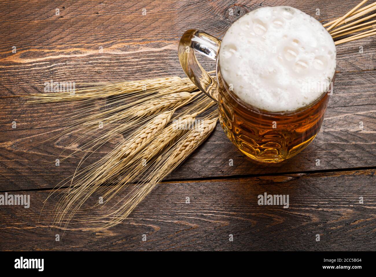 vista dall'alto della pinta di birra con schiuma su tavolo di legno con spighe di grano. Foto Stock