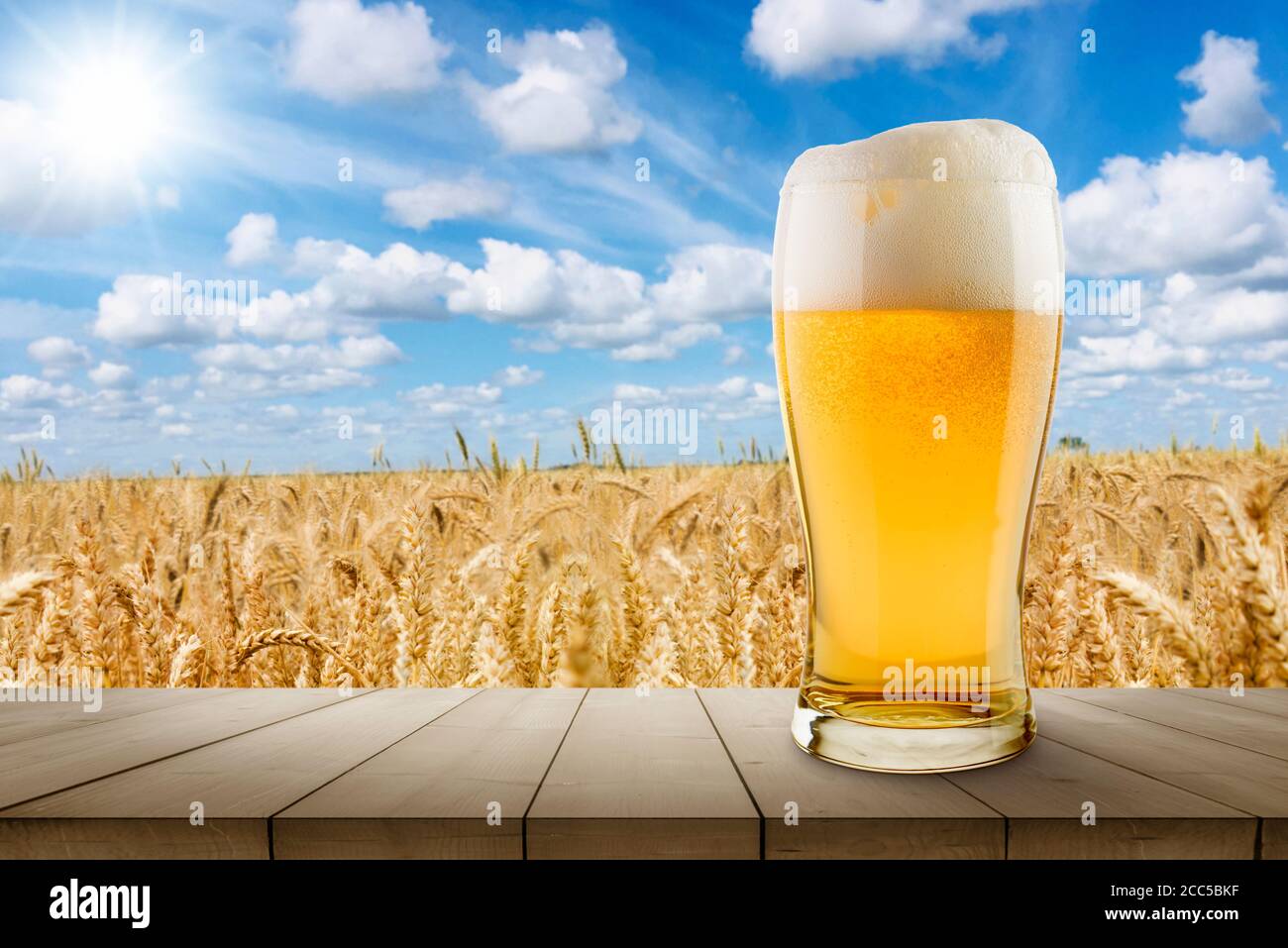 bicchiere di birra bionda su tavolo di legno con grano soleggiato campo sullo sfondo Foto Stock