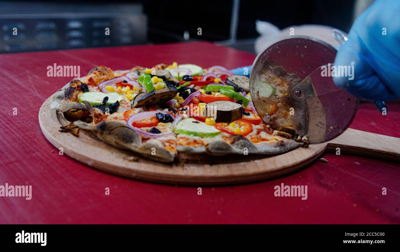 Colpo di primo piano di una persona che taglia la pizza con un taglierina per pizza su un piatto di legno Foto Stock