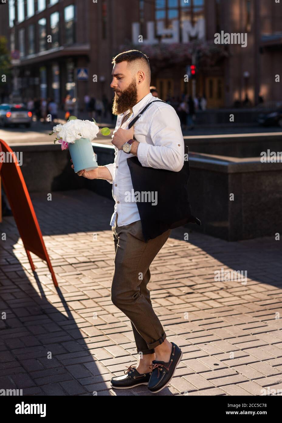 Kiev, Ucraina - 11 luglio 2020. Khreshchatyk str. Bello hipster dell'uomo bearded fiducioso che tiene la scatola del fiore del regalo dei fiori bianchi sulla strada della città Foto Stock