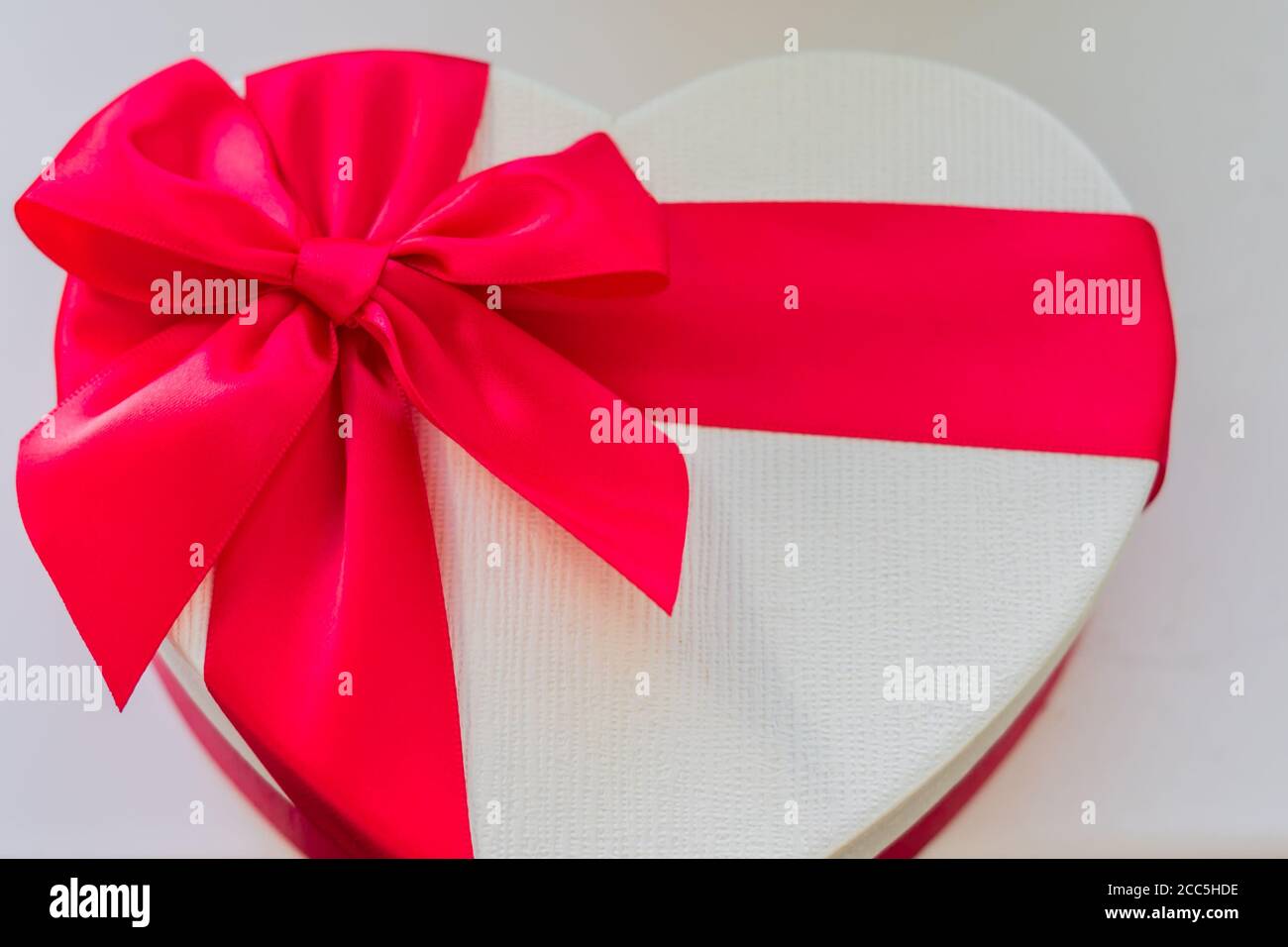 primo piano della confezione regalo bianca a forma di cuore con arco rosso e nastro, vista dall'alto Foto Stock
