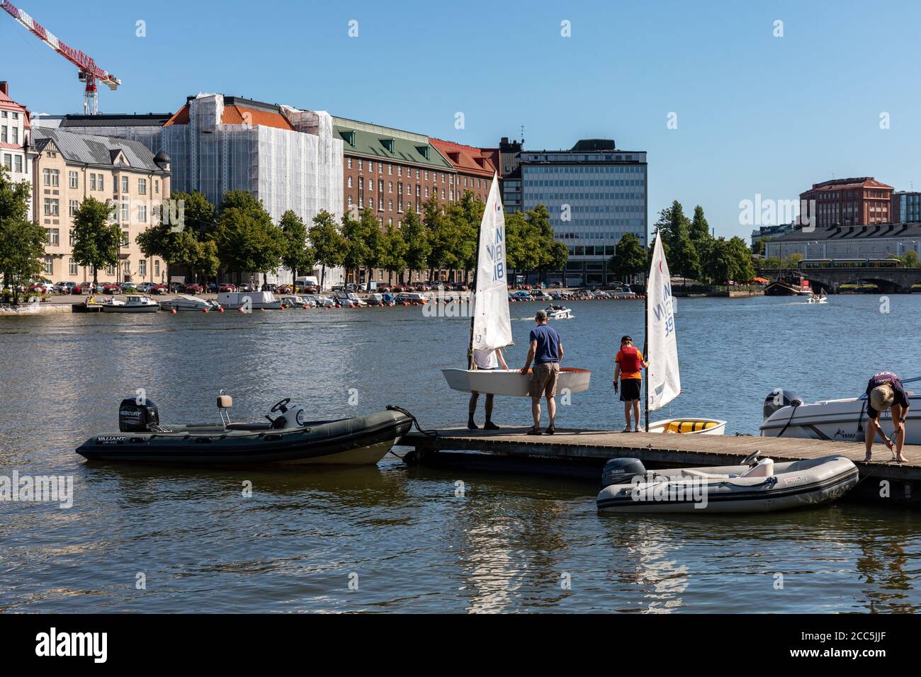 Uomini che trasportano un leggero skiff a vela su un molo a Kaisaniemi Bay a Helsinki, Finlandia Foto Stock