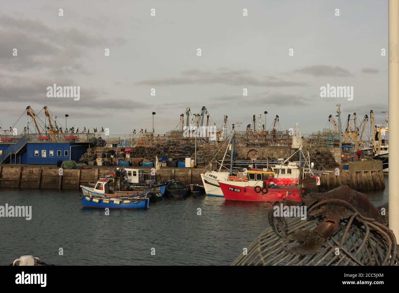 Barche da pesca ormeggiate lungo banchina con granchi impilati sul molo, Brixham, Devon, UK Foto Stock