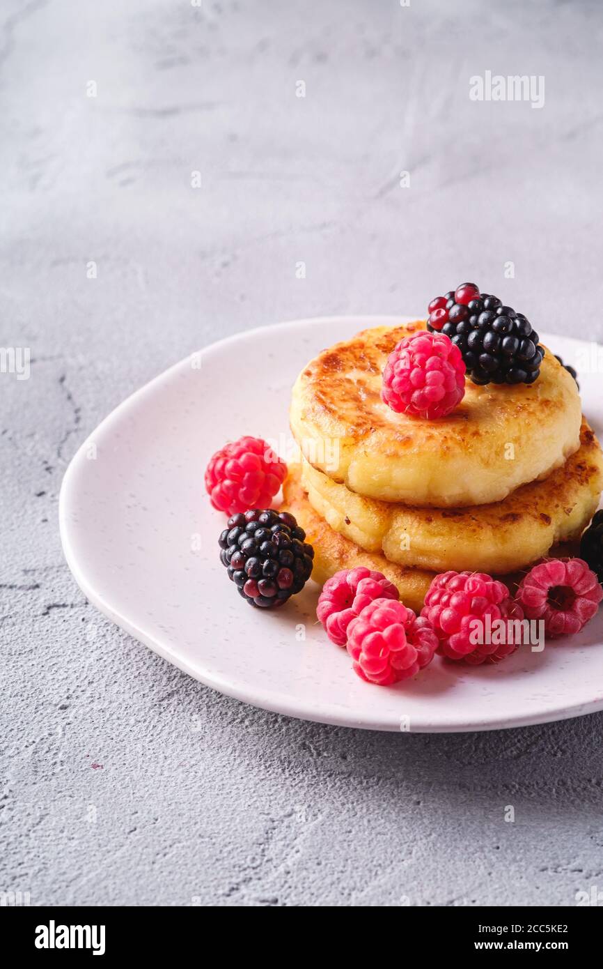 Frittelle di formaggio cottage, frittelle di cagliata dessert con lampone e bacche di mora in piastra su fondo di pietra in cemento, vista angolare Foto Stock