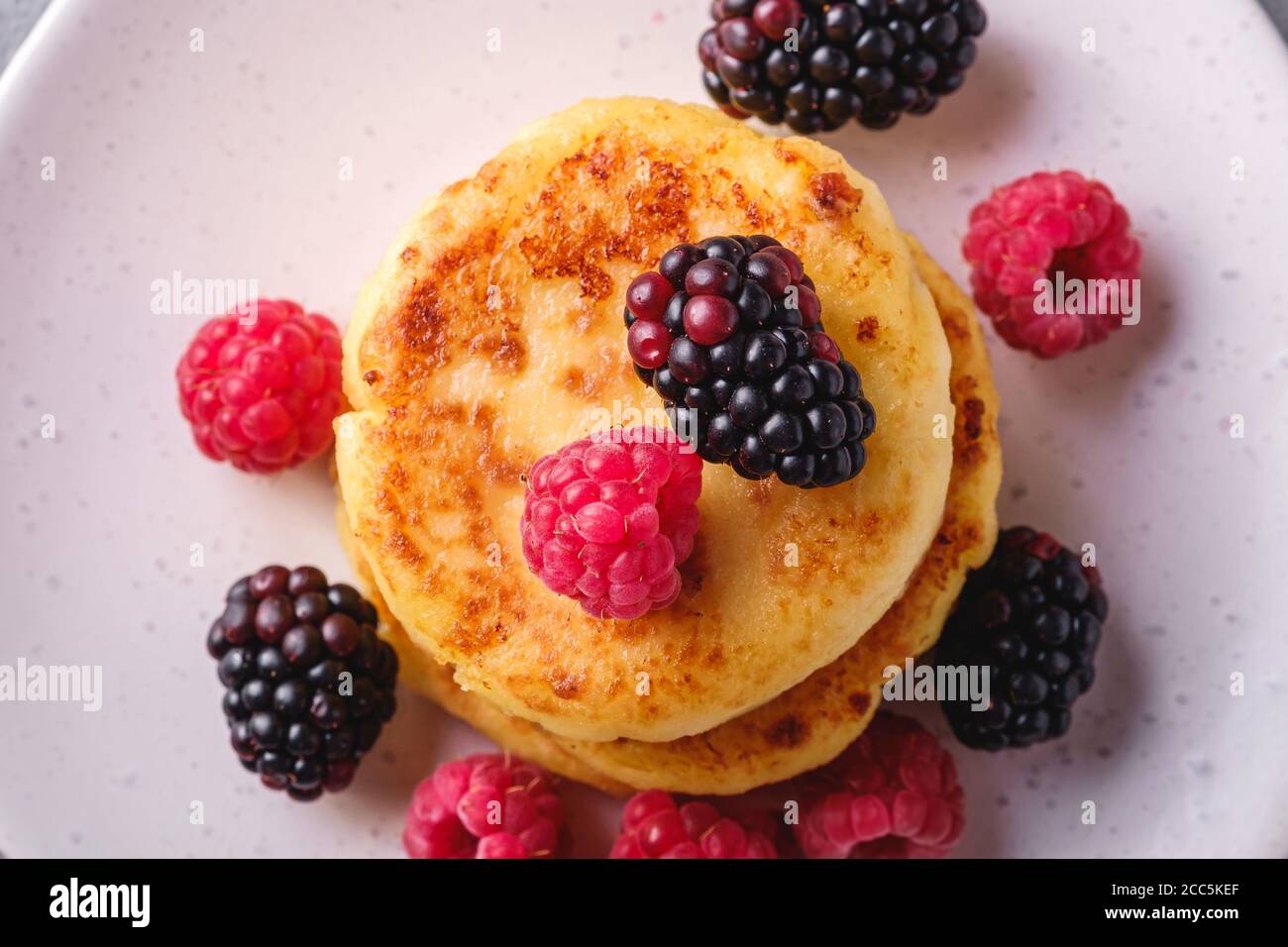 Frittelle di formaggio cottage, frittelle di cagliata dessert con lampone e frutti di mora in piastra su fondo di pietra cemento, macro vista dall'alto Foto Stock