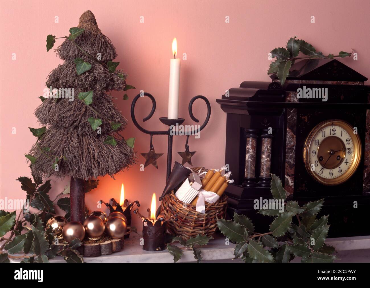 Candele, cesto di spezie natalizie e albero di fuoco su un pezzo di legno accanto al grande orologio Foto Stock