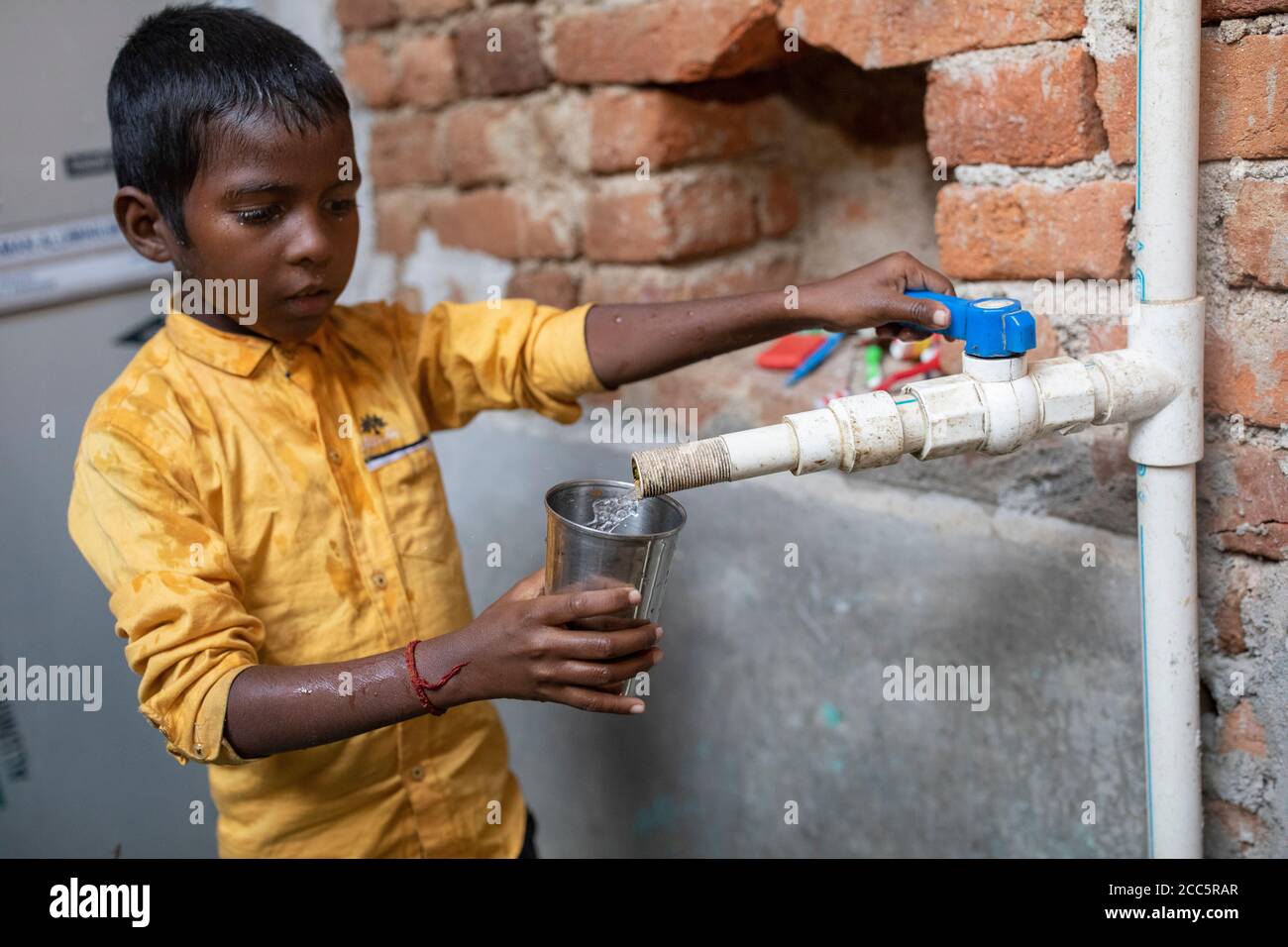 Un ragazzo di otto anni beve acqua dal nuovo rubinetto che sua madre aveva installato recentemente nella casa della famiglia a Bihar, India. Foto Stock