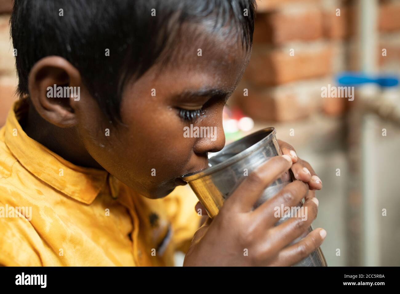 Un ragazzo di otto anni beve acqua dal nuovo rubinetto che sua madre aveva installato recentemente nella casa della famiglia a Bihar, India. Foto Stock