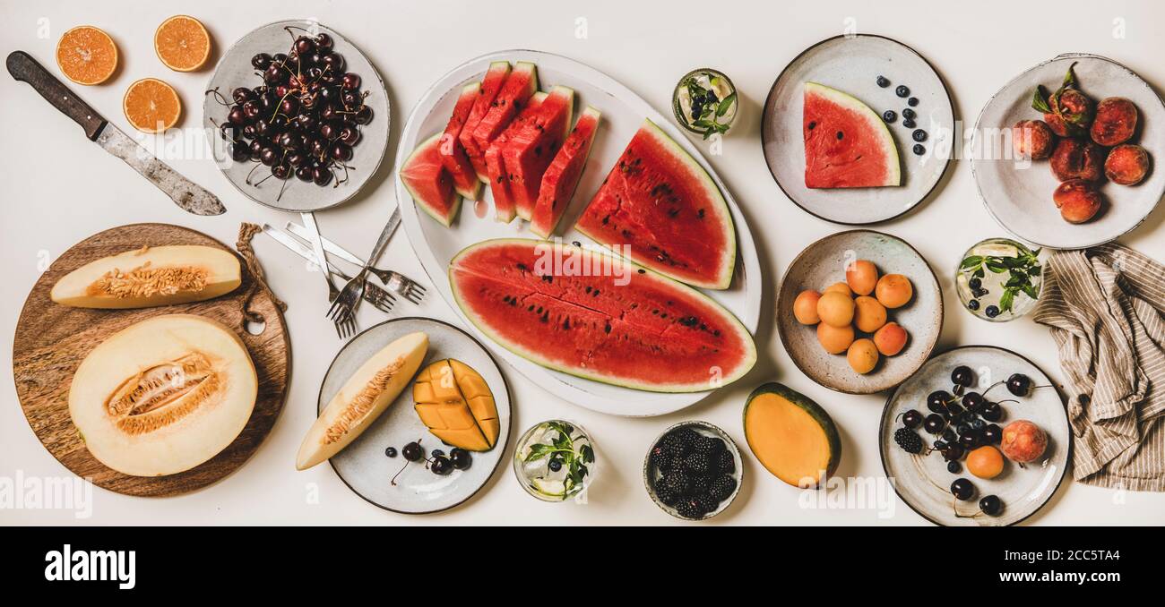 Estate frutta tropicale vegan party tavolo. Piatto-lay di tavola estate pranzo impostazione con vari frutti, bacche, anguria e limonata su bianco semplice Foto Stock