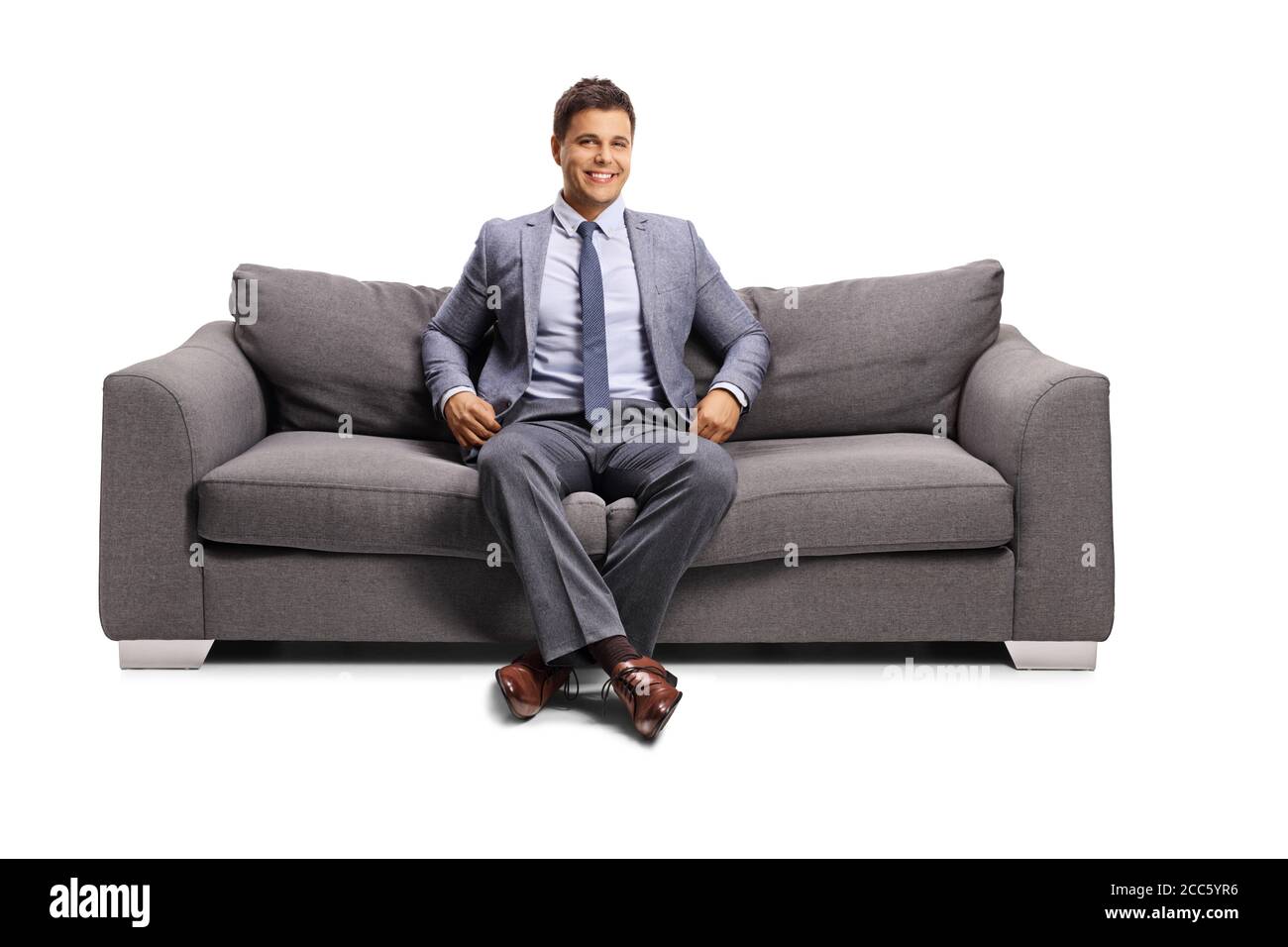 Uomo in abiti eleganti seduto su un divano e sorridente isolato su sfondo bianco Foto Stock