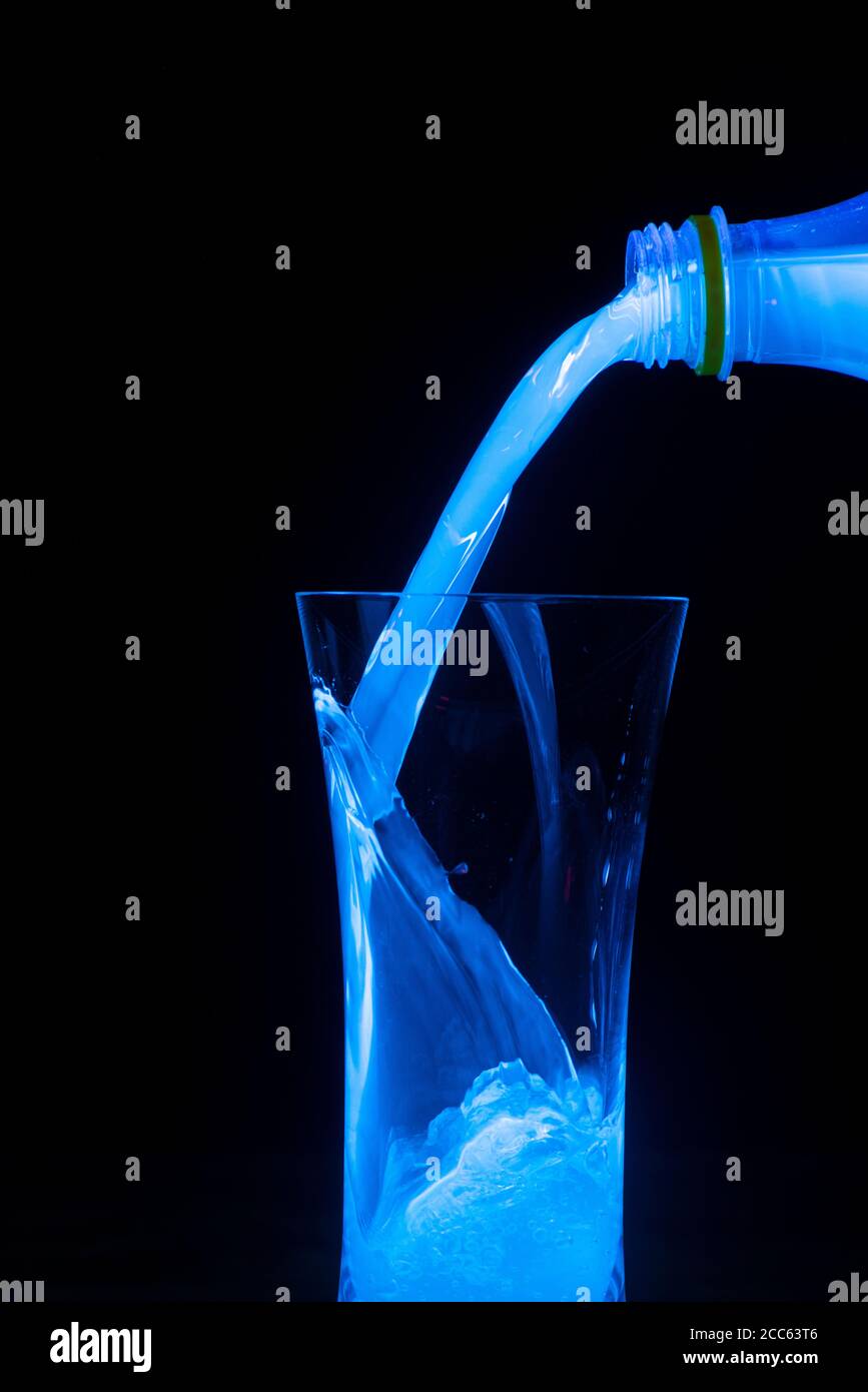 Acqua tonica che viene versata su ghiaccio. Fluorescenza UV Foto Stock