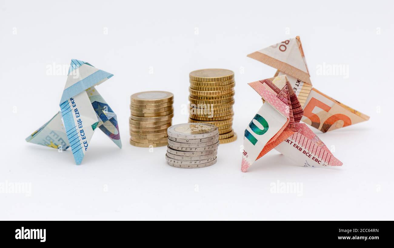 Tre uccelli origami fatti di banconote da 10, 20 e 50 euro, intorno a pile di monete in euro, fondo bianco Foto Stock