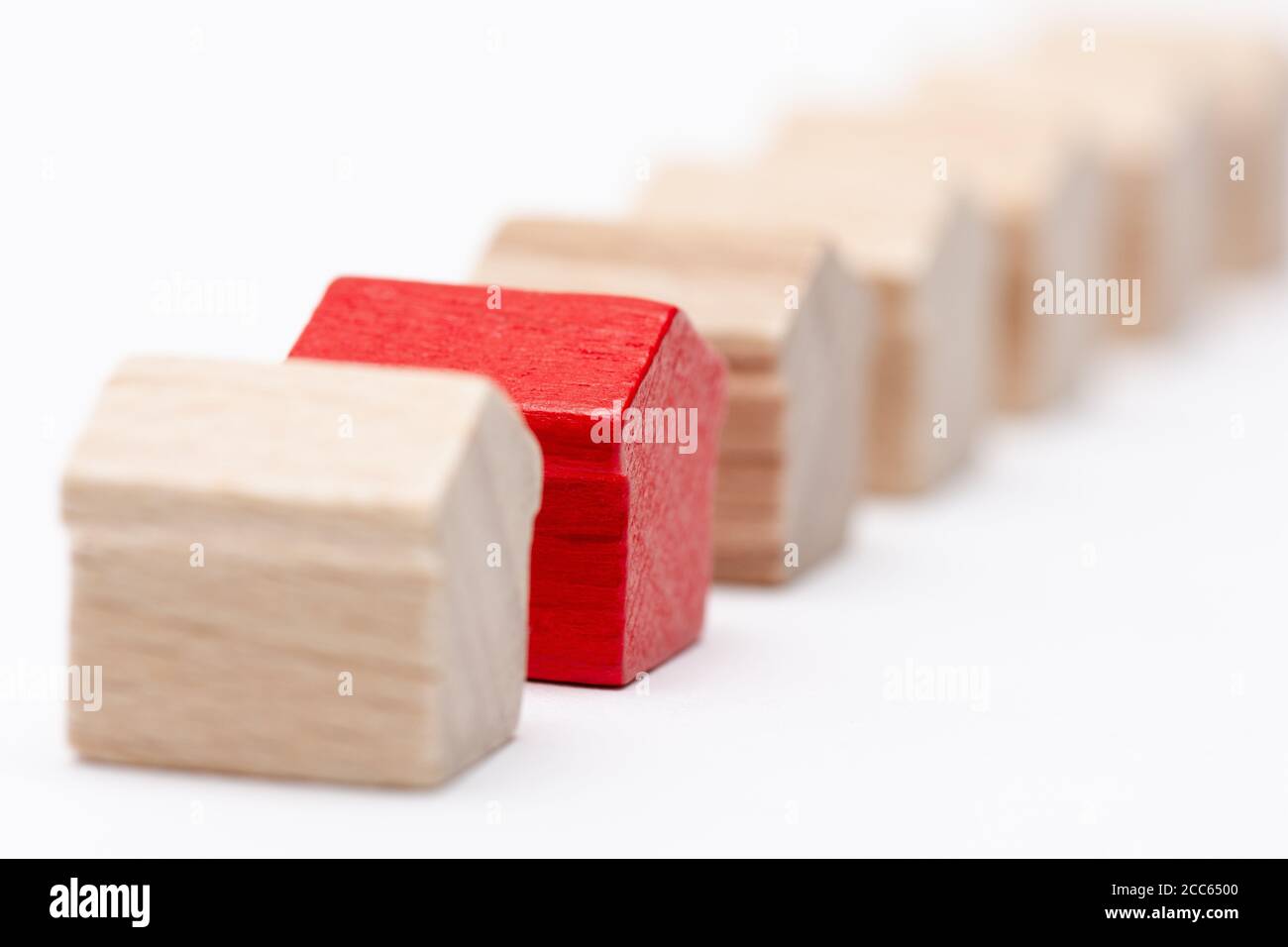 Piccole case di giocattoli in legno in una fila, una di loro dipinta rosso, sfondo bianco Foto Stock