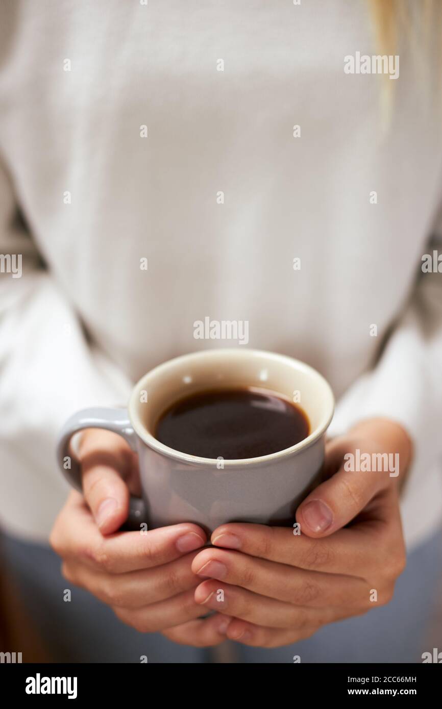 Primo piano di una mano di donna che tiene una tazza di caldo caffè che indossa un maglione Foto Stock