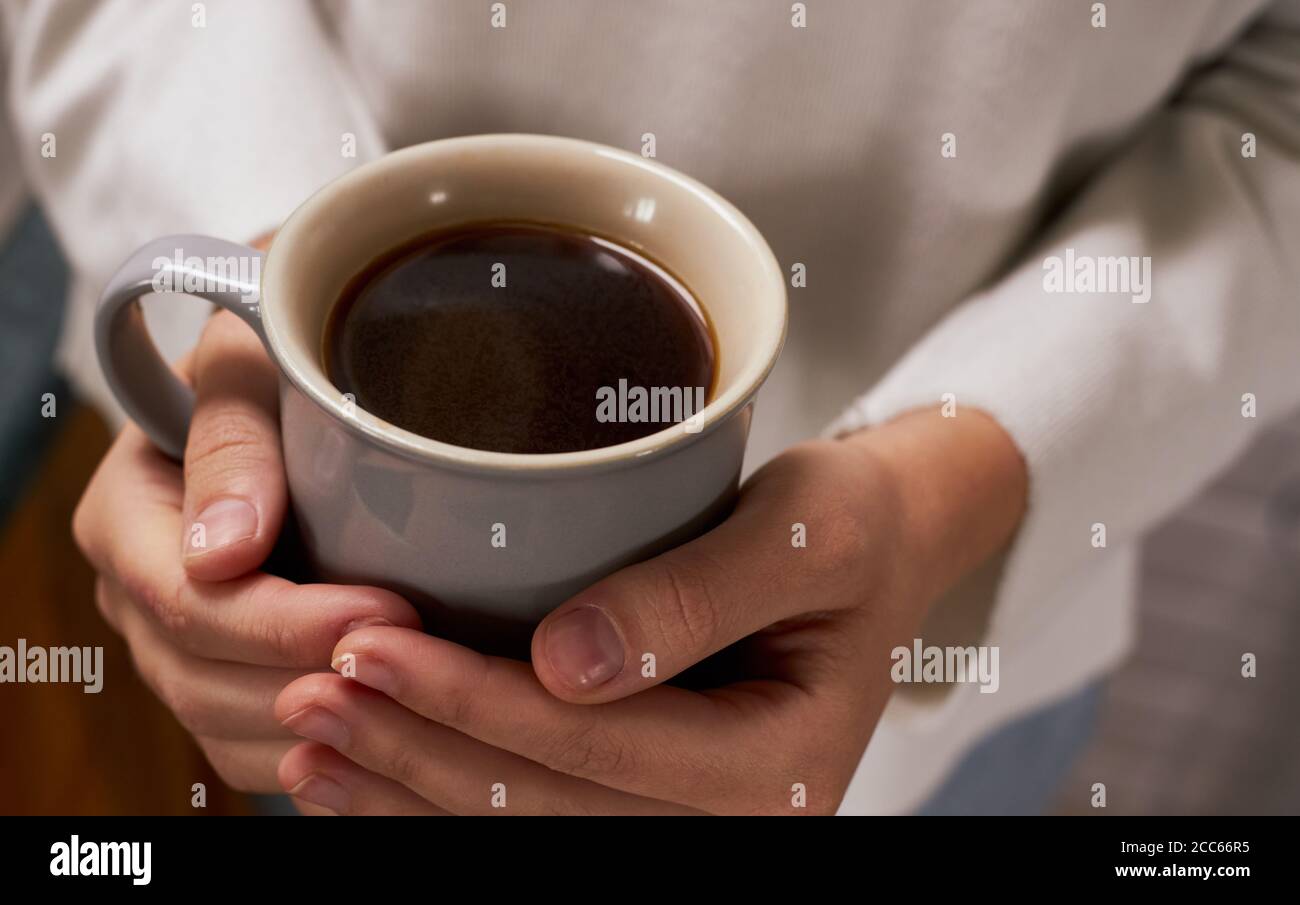 Primo piano di una mano di donna che tiene una tazza di caldo caffè che indossa un maglione Foto Stock