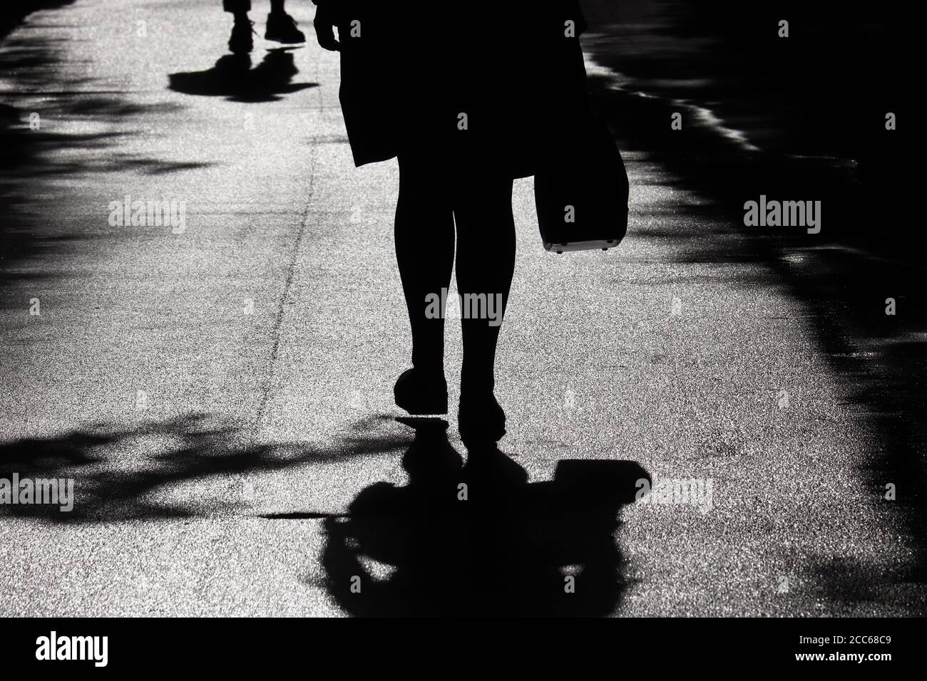 Silhouette e ombra di donna che cammina su una strada. Gambe femminili su un marciapiede, concetto di quarantena in città durante la pandemia del coronavirus Foto Stock