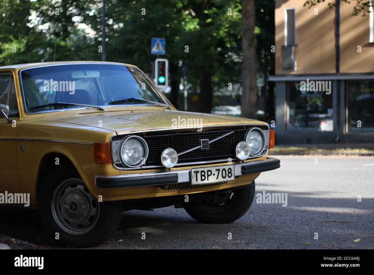 Volvo classico vecchio colore giallo con fari tondi sotto qualche ombra con un semaforo verde sullo sfondo. Preso a Tampere, Finlandia. Foto Stock