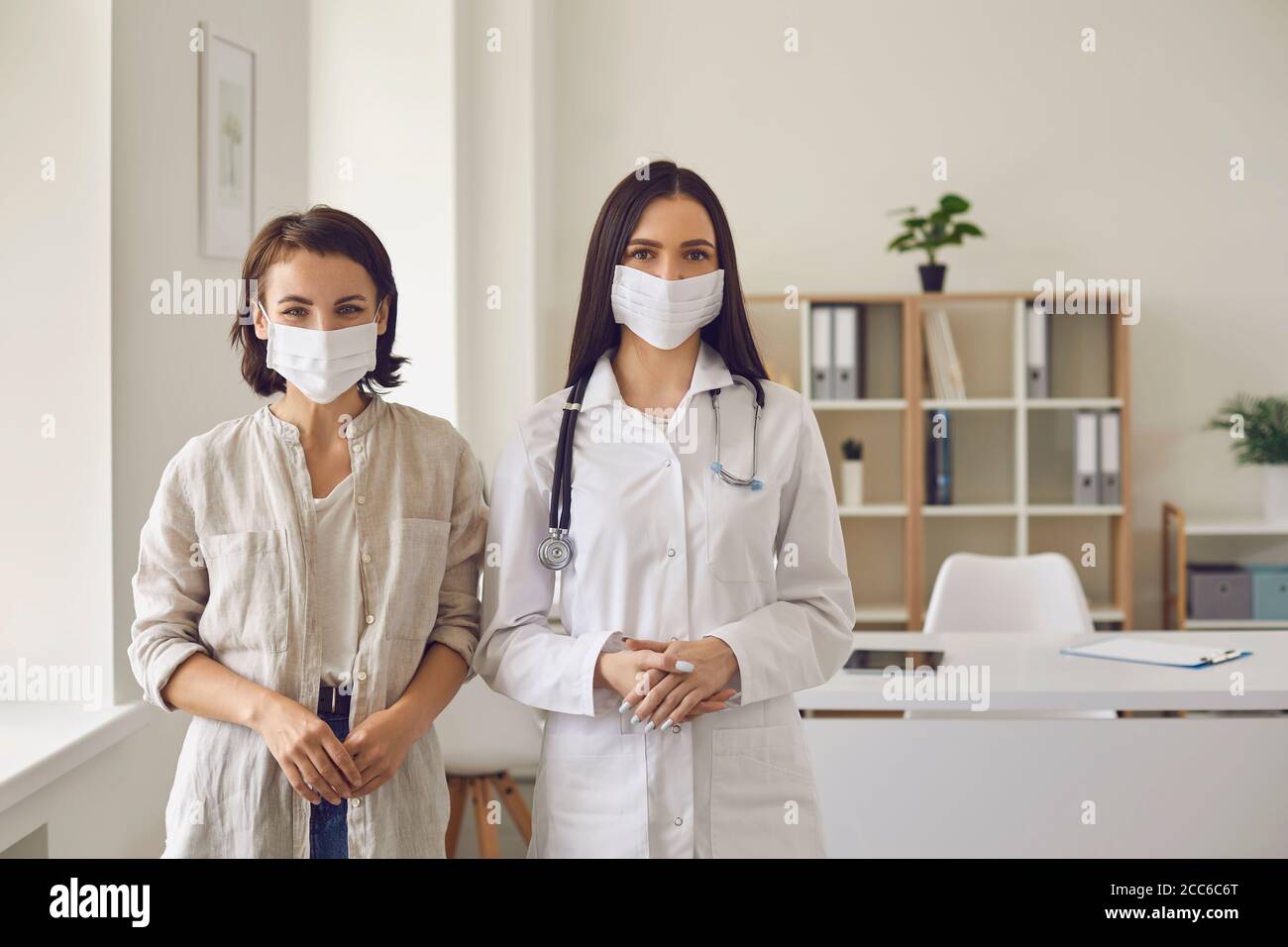 Ritratto di un medico millenario e di un paziente che indossa maschere protettive presso l'ufficio medico. Combattere le malattie virali Foto Stock