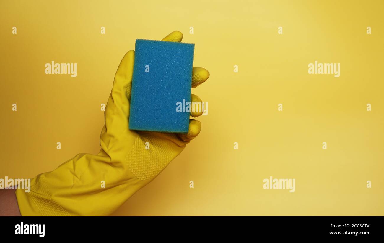 Spugna per lavare piatti in mano. Indossate un guanto in lattice isolato. Una mano in un guanto contiene una spugna per il lavaggio e la pulizia su sfondo giallo Foto Stock