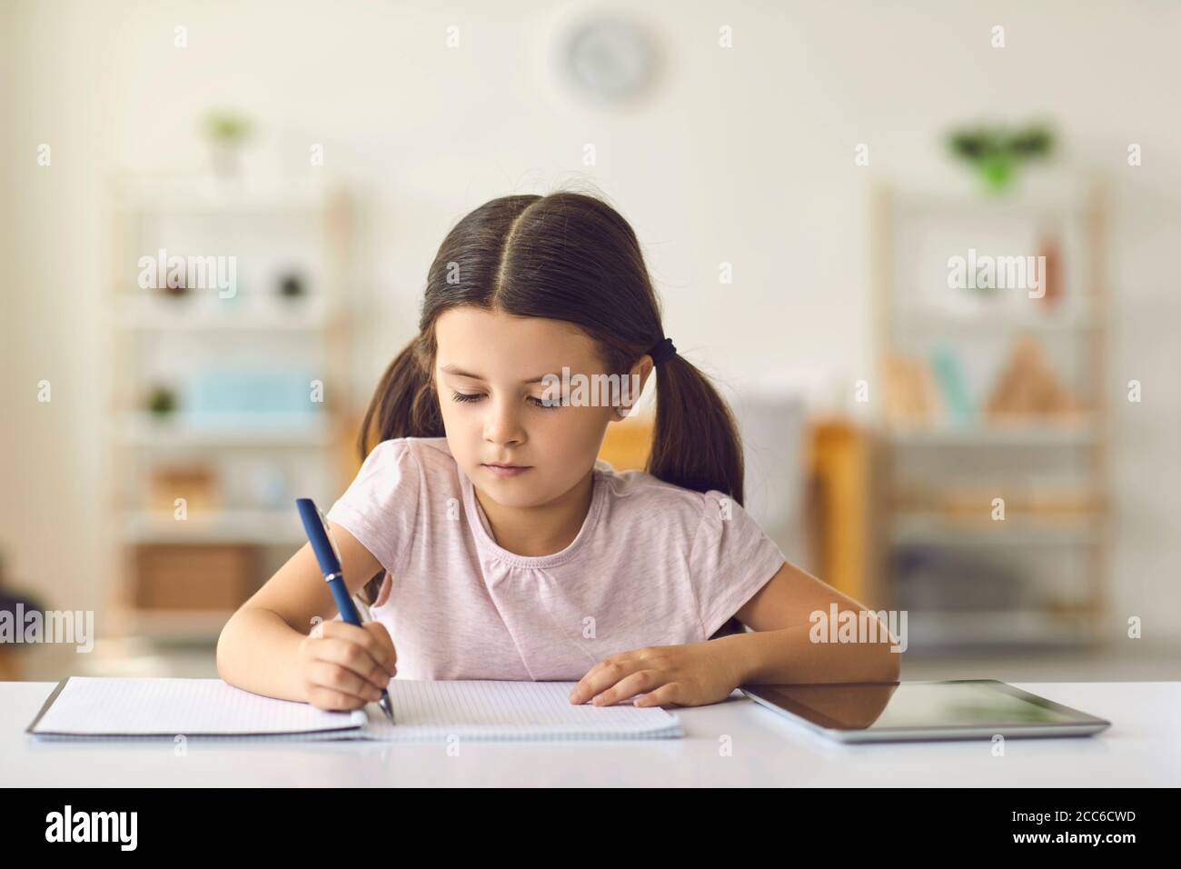 Educazione online per i bambini. Studentessa scrive in un taccuino l'incarico dell'insegnante a casa. Foto Stock