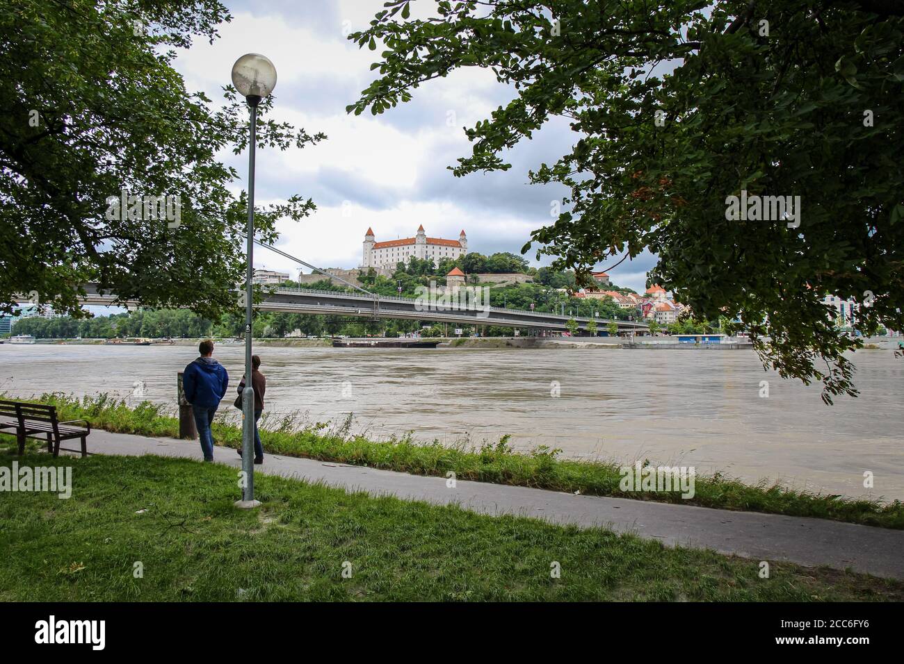 Bratislava, Slovacchia - 5 luglio 2020: Persone che camminano lungo un sentiero sul Danubio a Bratislava, con il Castello sulla collina sullo sfondo Foto Stock